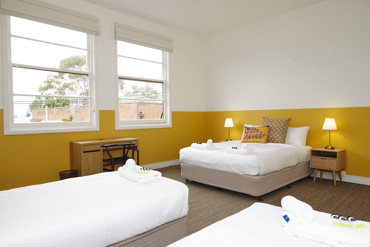 A hotel room with two beds, a desk, and a window with a view of the outside.