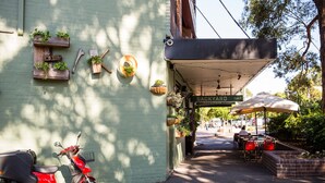 Un bâtiment à la façade verdoyante, un scooter rouge garé devant, et une enseigne indiquant « CUISINE D’EXTÉRIEUR ».