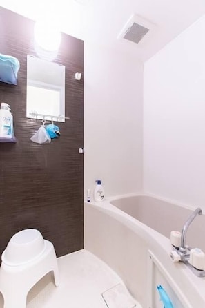 Un baño con una bañera blanca, un inodoro blanco y un taburete pequeño blanco.