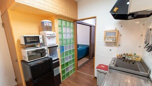 A compact kitchen with a microwave, toaster, and coffee machine, a small sink, and a storage area with green crates. - YokohamaKannai HouseBar (Yokohama)