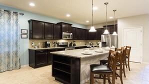 A modern kitchen with dark wood cabinets, stainless steel appliances, a granite countertop island, and pendant lighting.