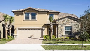 A two-story house with a beige facade, a stone exterior on the right side, a garage, and palm trees in the front yard.