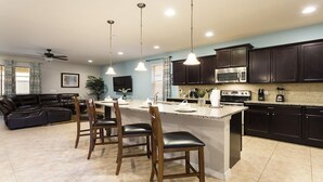 A modern kitchen with dark wood cabinets, a stainless steel microwave, and a granite countertop. There are three pendant lights above the island, and a ceiling fan is visible in the background.