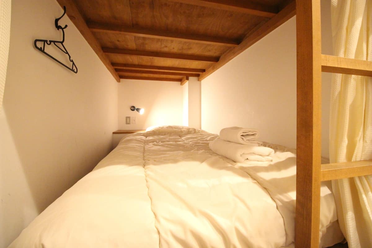 A single bed with a wooden headboard, a hanging coat rack, and a bedside lamp.