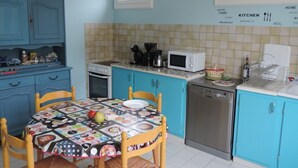 A kitchen with blue cabinets, a microwave, a dishwasher, and a table with a colorful tablecloth. - beautiful ronçoise villa for 7 people near the beach and shops (Ronce-les-Bains)