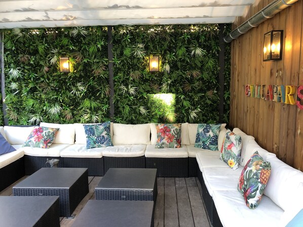 A cozy outdoor seating area with a white cushioned sofa, black woven tables, and a lush green wall backdrop. - Villa Parisiata Swimming pool, Sauna, Garden and Fitness
Exceptional location! (Puteaux)