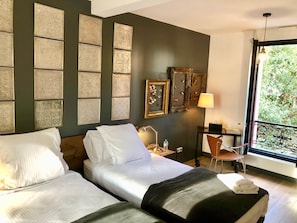 A hotel room with two beds, a desk with a chair, a lamp, and artwork on the walls. - Villa Parisiata Swimming pool, Sauna, Garden and Fitness
Exceptional location! (Puteaux)