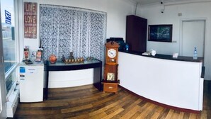 Una habitación con piso de madera, un mostrador de recepción blanco, un reloj y un ventanal con cortinas florales.