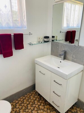 A bathroom with a white sink, a mirror, and a tiled floor. There are two red towels hanging on a towel rack. - Tamworth Budget Motel (South Tamworth)