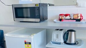Una kitchenette compacta con microondas, un refrigerador pequeño, un tostador y una tetera sobre una encimera blanca.