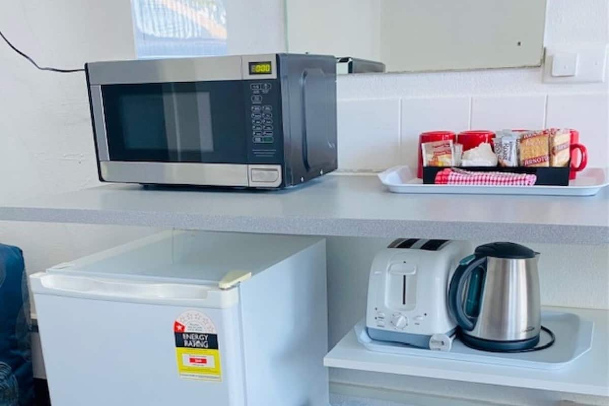 A compact kitchenette with a microwave, a small refrigerator, a toaster, and a kettle on a white countertop.