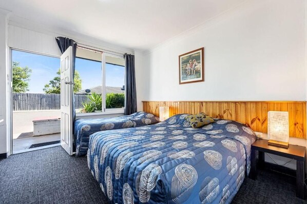 Un dormitorio con dos camas, un cabecero de madera, una mesita de noche, una ventana con cortinas y un cuadro en la pared.