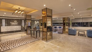 Una moderna hall d'albergo con reception, area salotto e uno specchio decorativo.