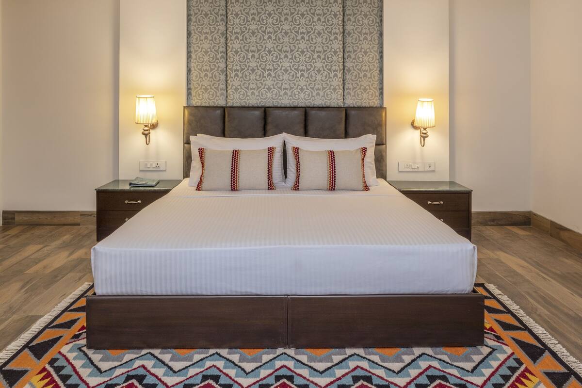 A large bed with a wooden headboard, two bedside lamps, and a patterned wall hanging above.