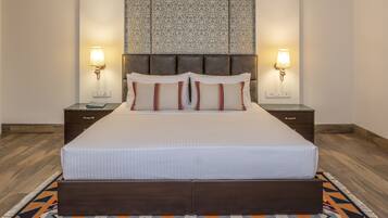 A large bed with a wooden headboard, two bedside lamps, and a patterned wall hanging above.