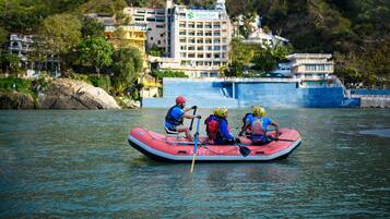 Un grupo de personas en una balsa inflable roja en un río, con edificios y árboles al fondo.