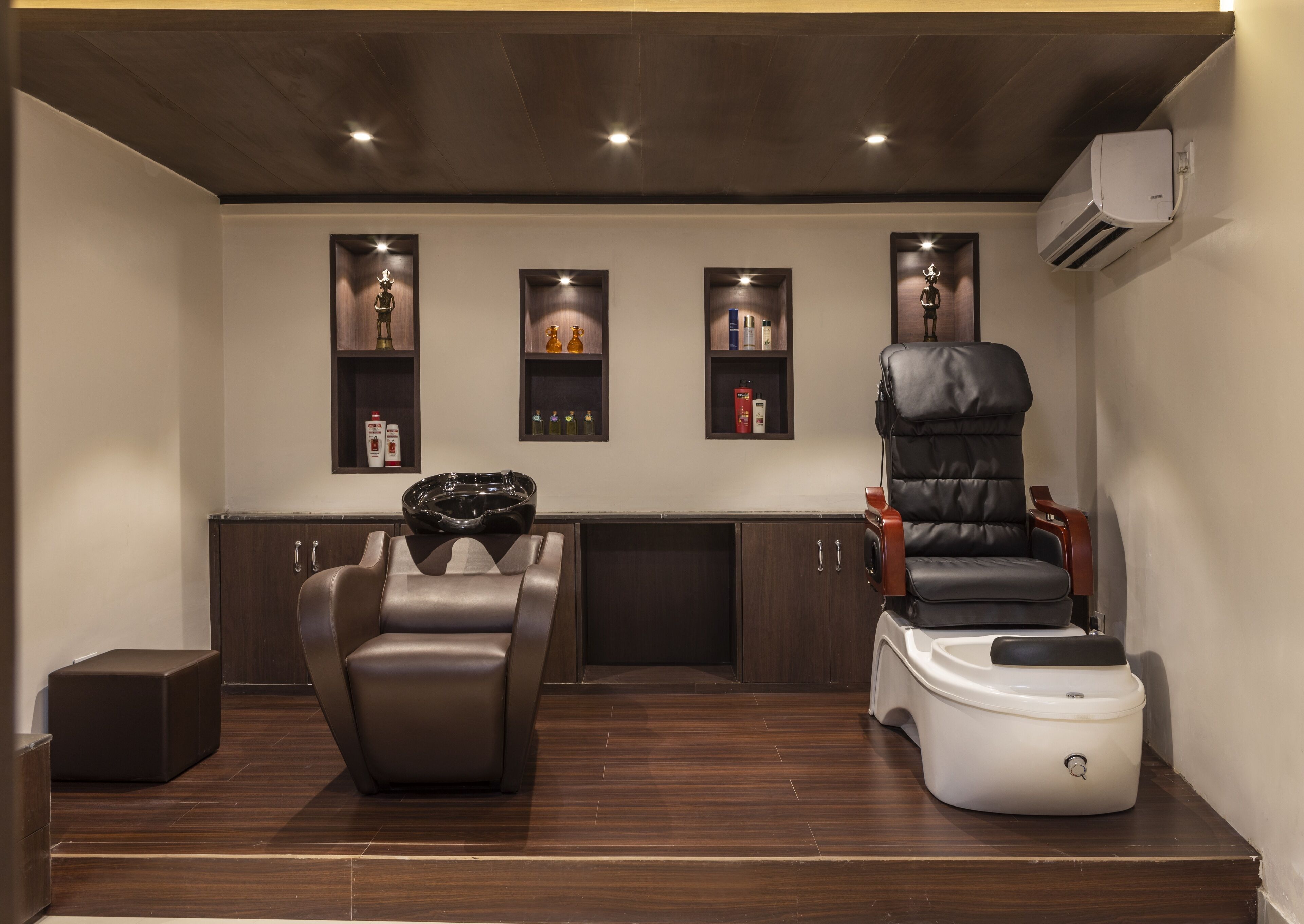Un cuarto de spa con una silla de masaje, un recipiente para pies y repisas con artículos de tocador.