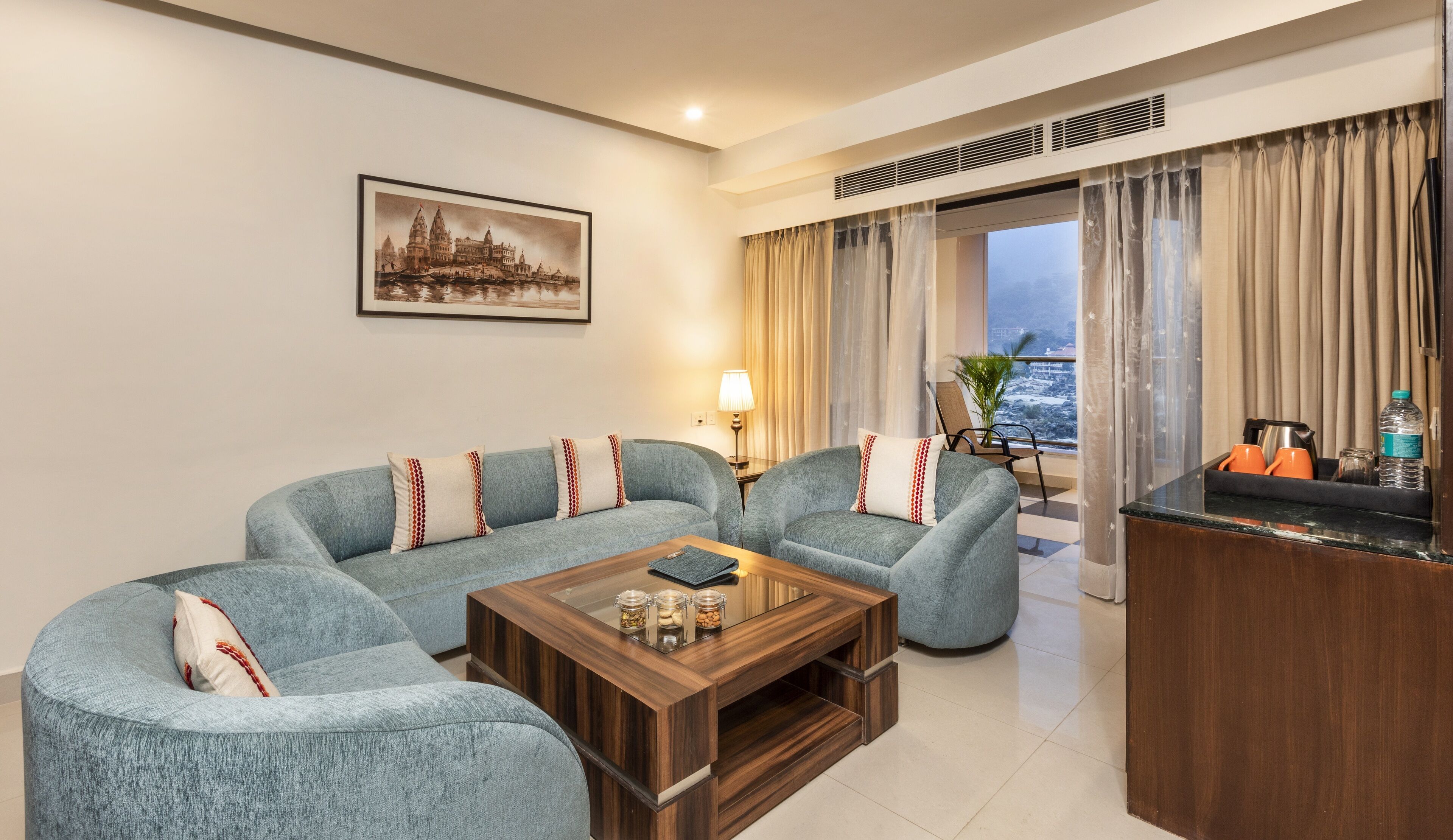 A living room with a sofa set, a coffee table, a lamp, and a view of the city through the window.