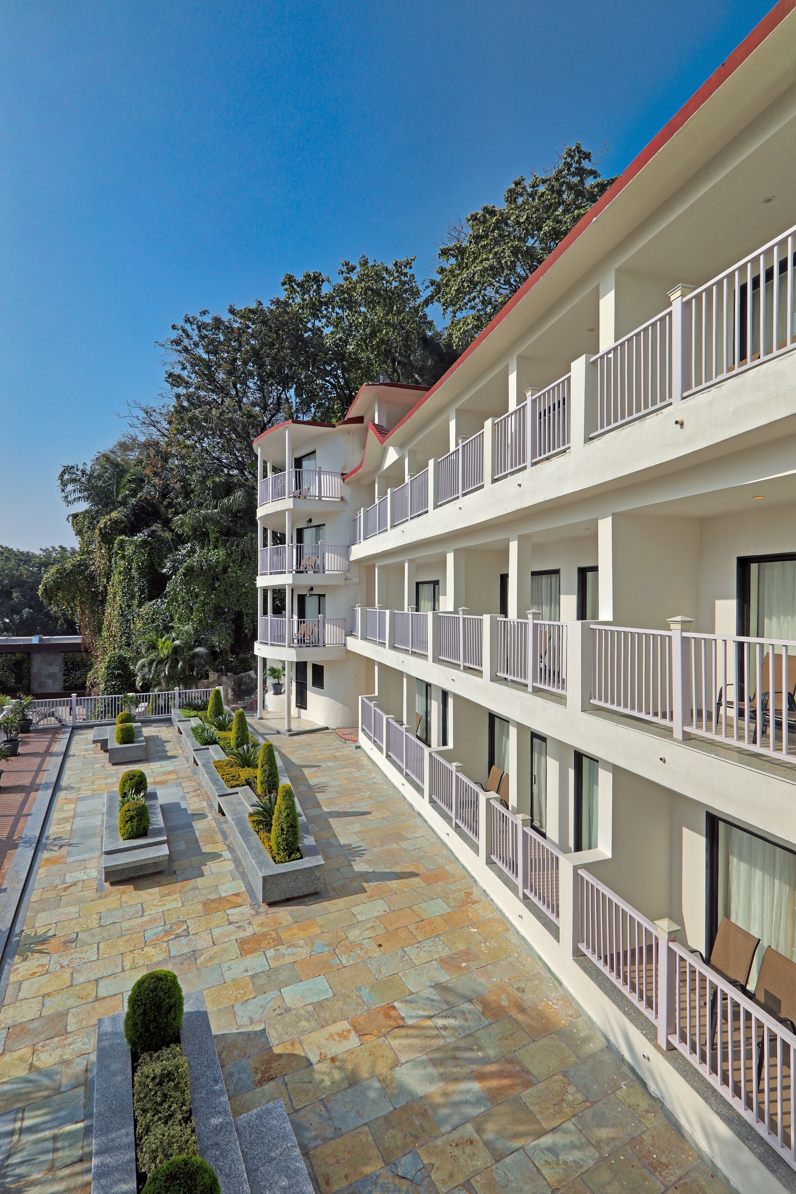 A multi-story hotel with balconies, a courtyard with stone paving, and surrounding greenery.
