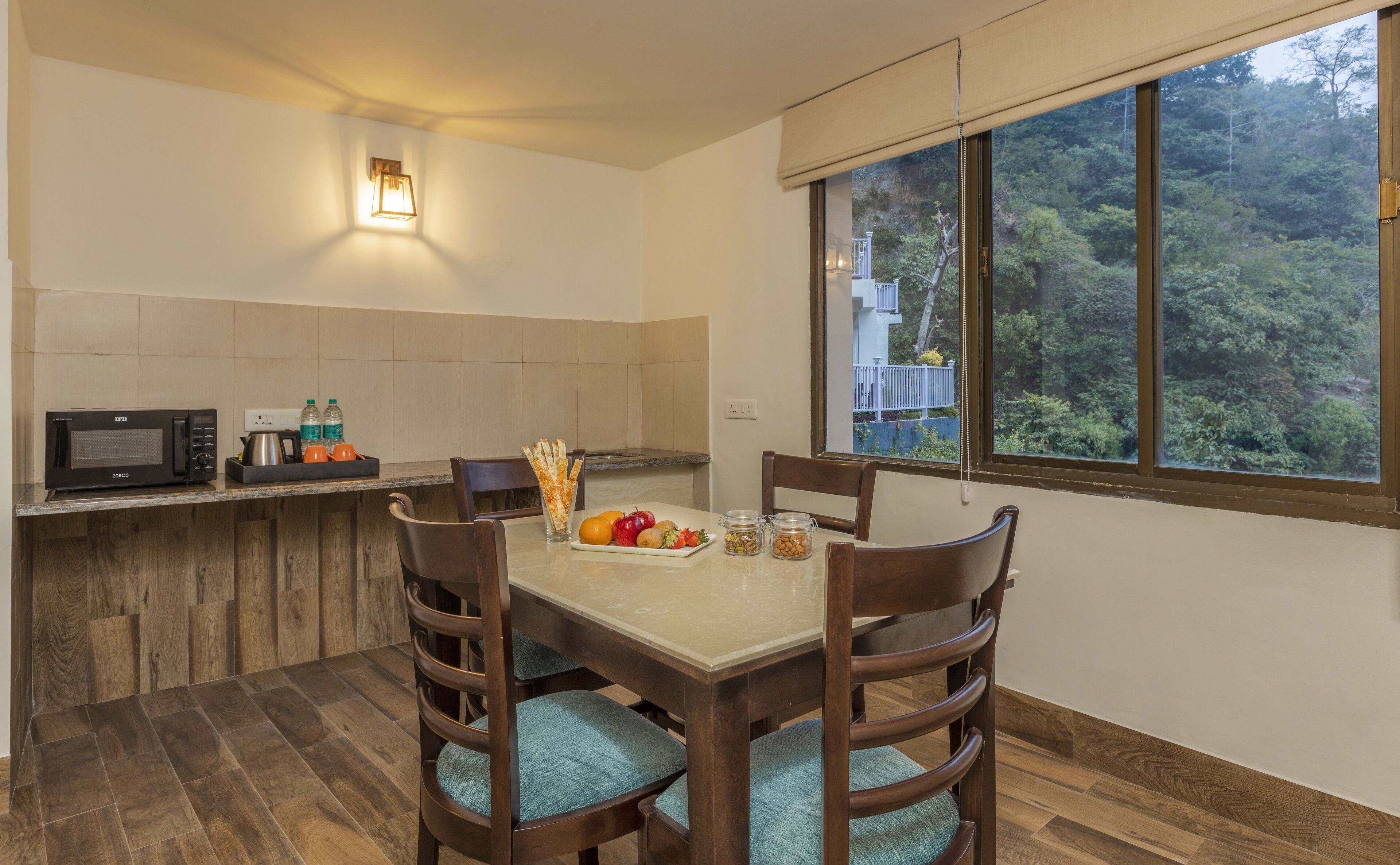 A kitchen with a dining table, chairs, a microwave, and a view of a forest through a window.
