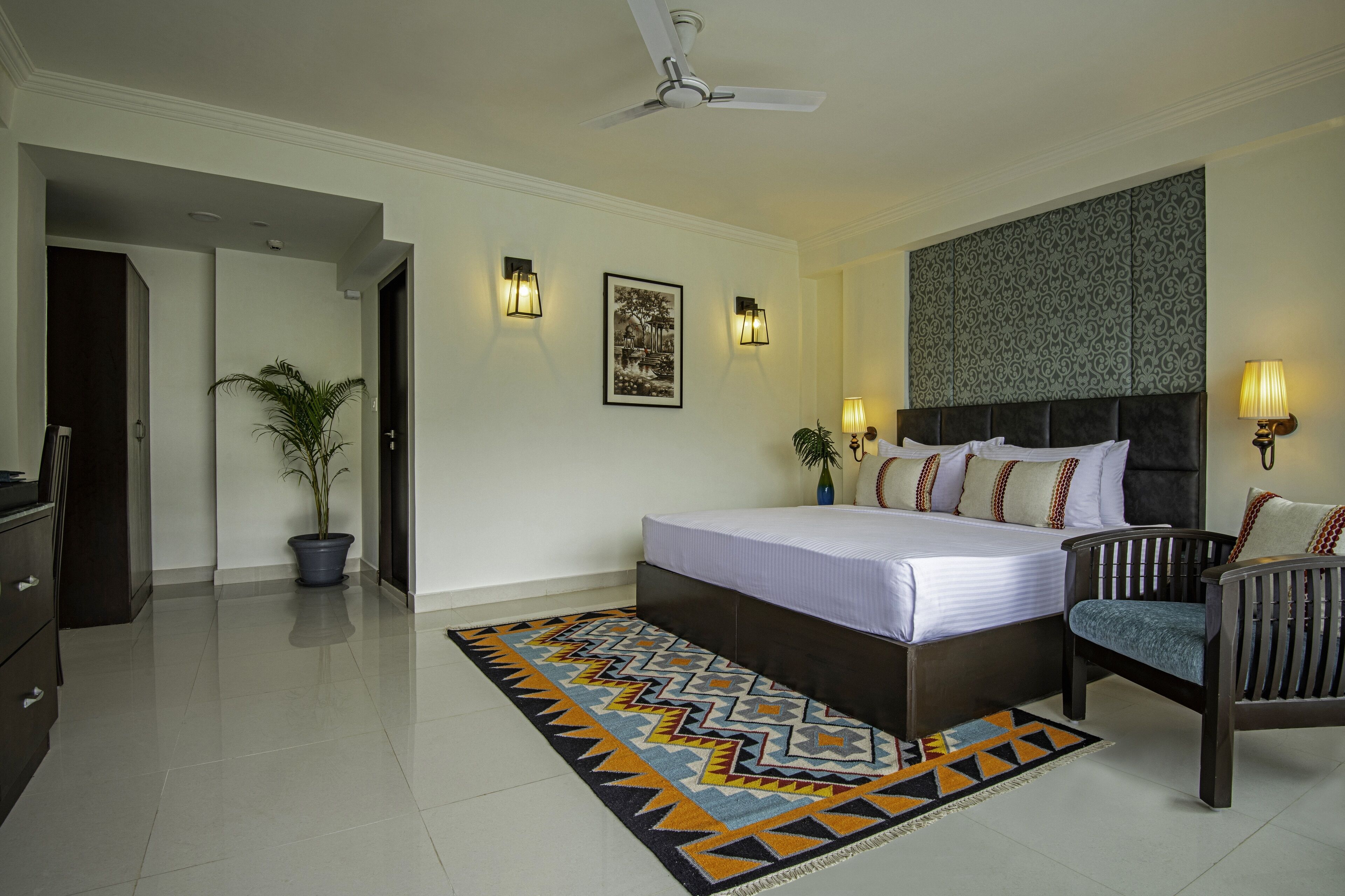 A bedroom with a bed, a chair, a potted plant, and wall-mounted lights.
