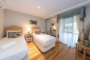 Et hotelværelse med to senge, et natbord med lampe, et spejl og et vindue med gardiner.