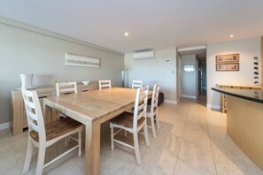 A dining area with a wooden table and white chairs, a kitchen area with a counter, and a hallway leading to another room.