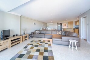 A modern living room with a sectional sofa, a flat-screen TV, a wooden entertainment unit, and a patterned rug.