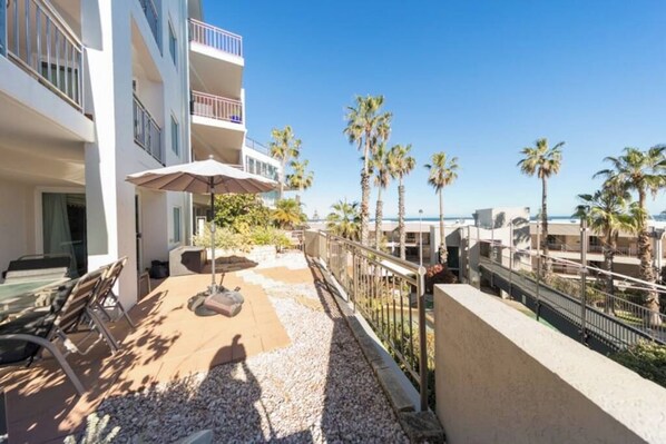 A hotel balcony with outdoor seating, palm trees, and a view of the sea.