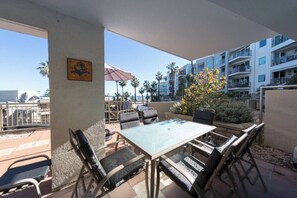 An outdoor patio with a table and chairs, a potted plant, and a view of a building with balconies.