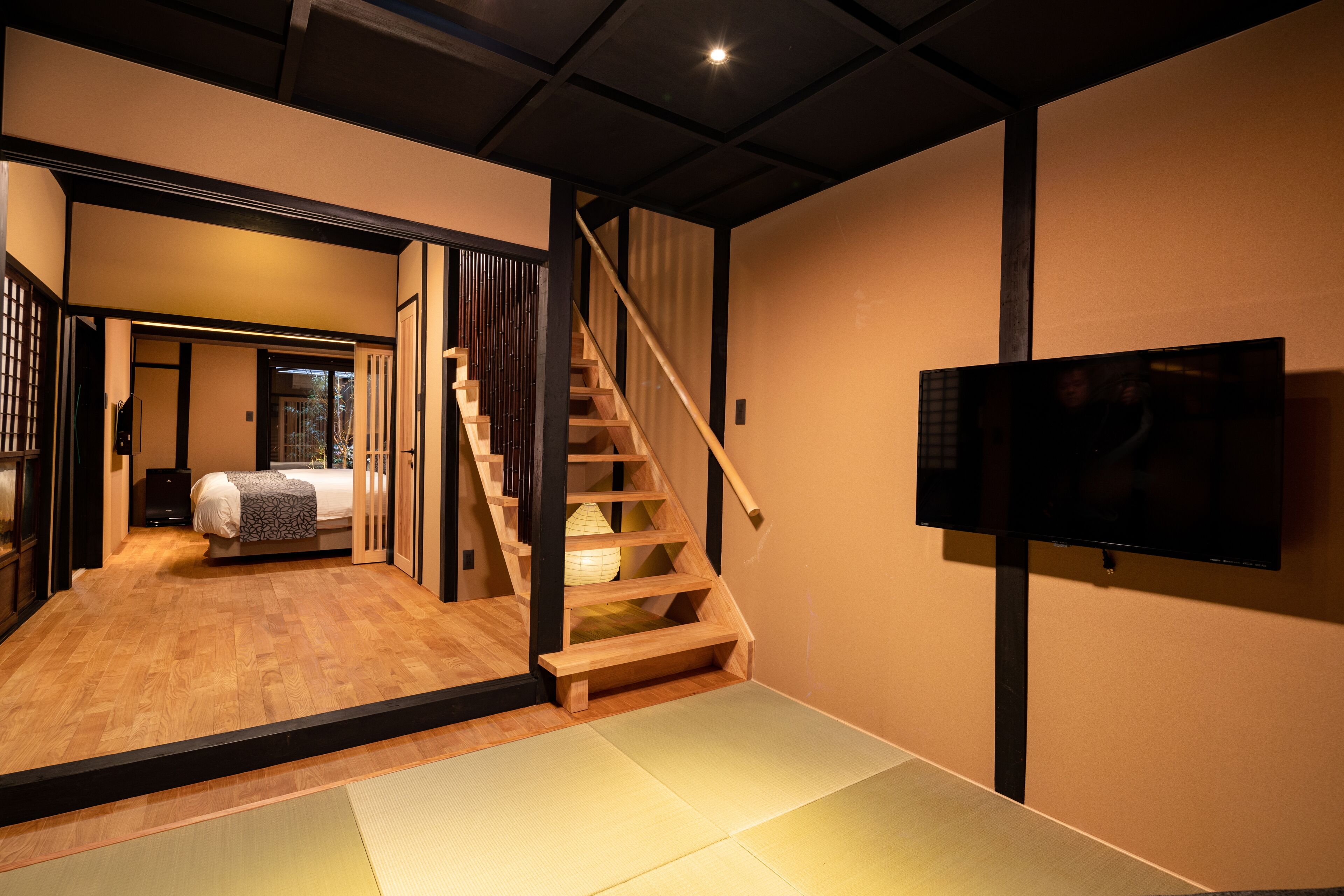 A modern interior with a wooden staircase, a bed, and a television mounted on the wall.