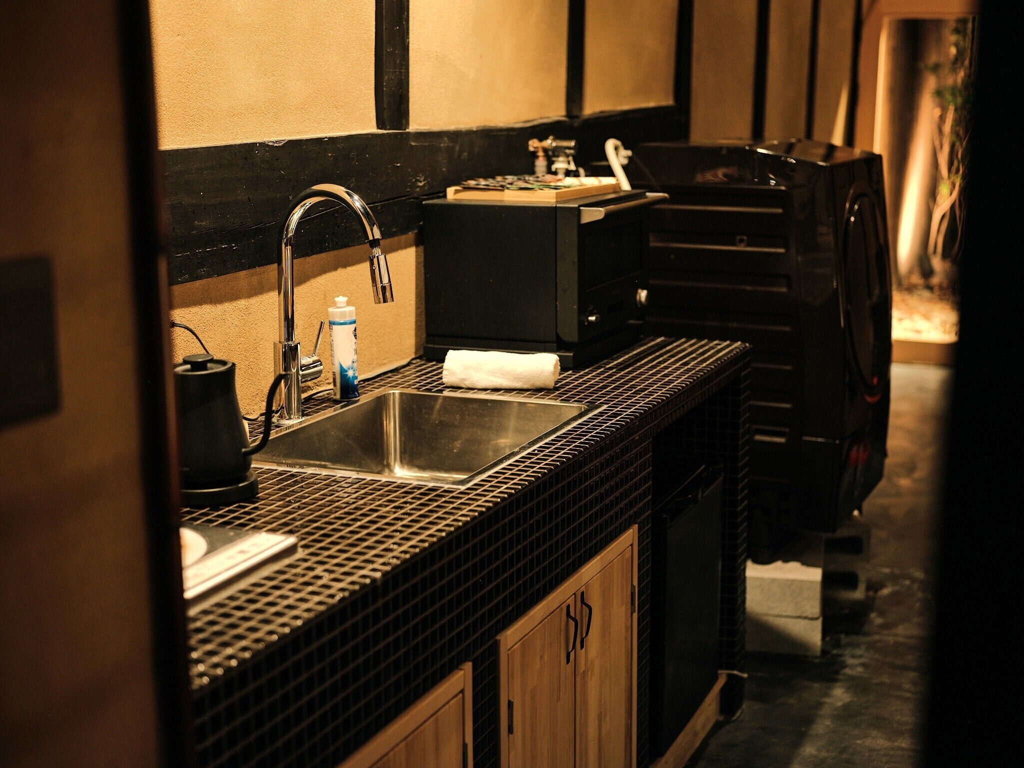 A kitchen with a black tiled countertop, a stainless steel sink, a coffee maker, and a toaster.