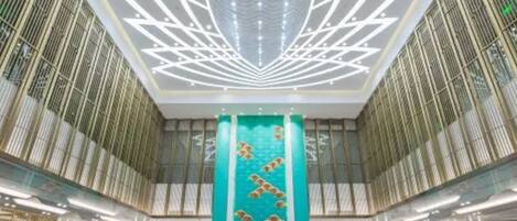 A modern interior with a central column featuring a decorative fish motif, surrounded by a symmetrical design with vertical lines and a lotus-like pattern on the ceiling.