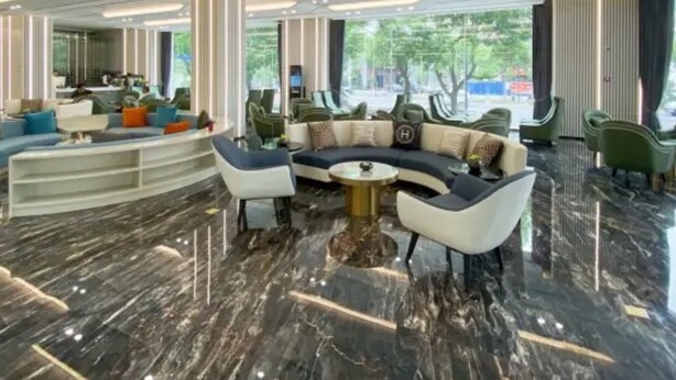 En moderne hotellobby med et buet siddeområde, marmorgulv og et højt loft med indbygget belysning.