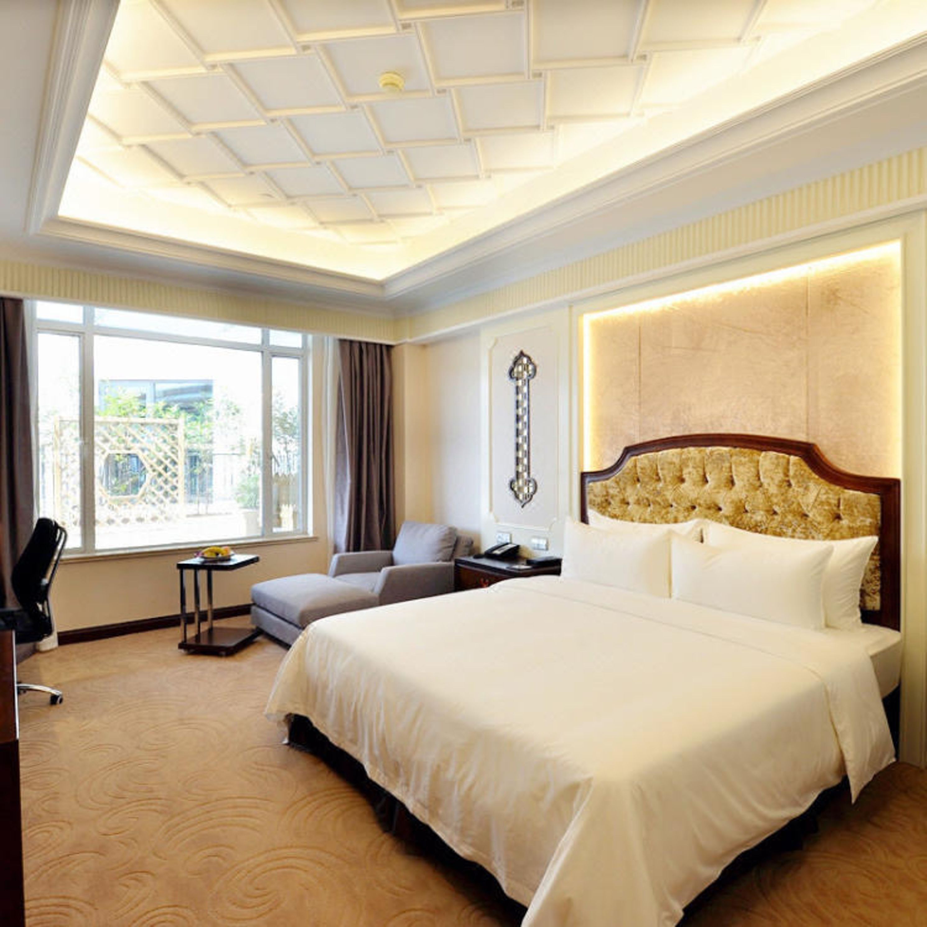 A hotel room with a large bed, a seating area with a chair and a small table, and a large window with curtains.