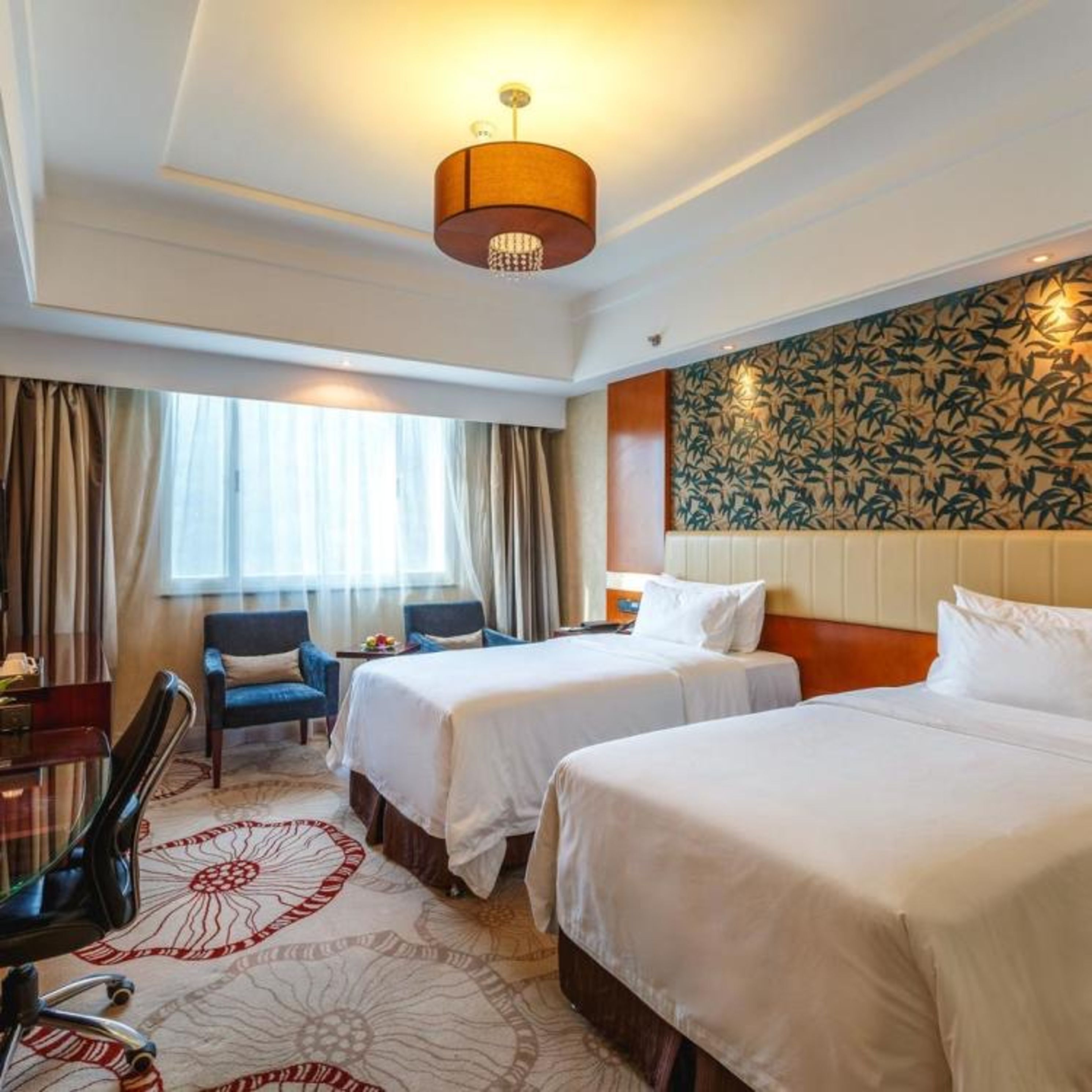 A hotel room with two beds, a desk, a chair, and a large window with curtains.