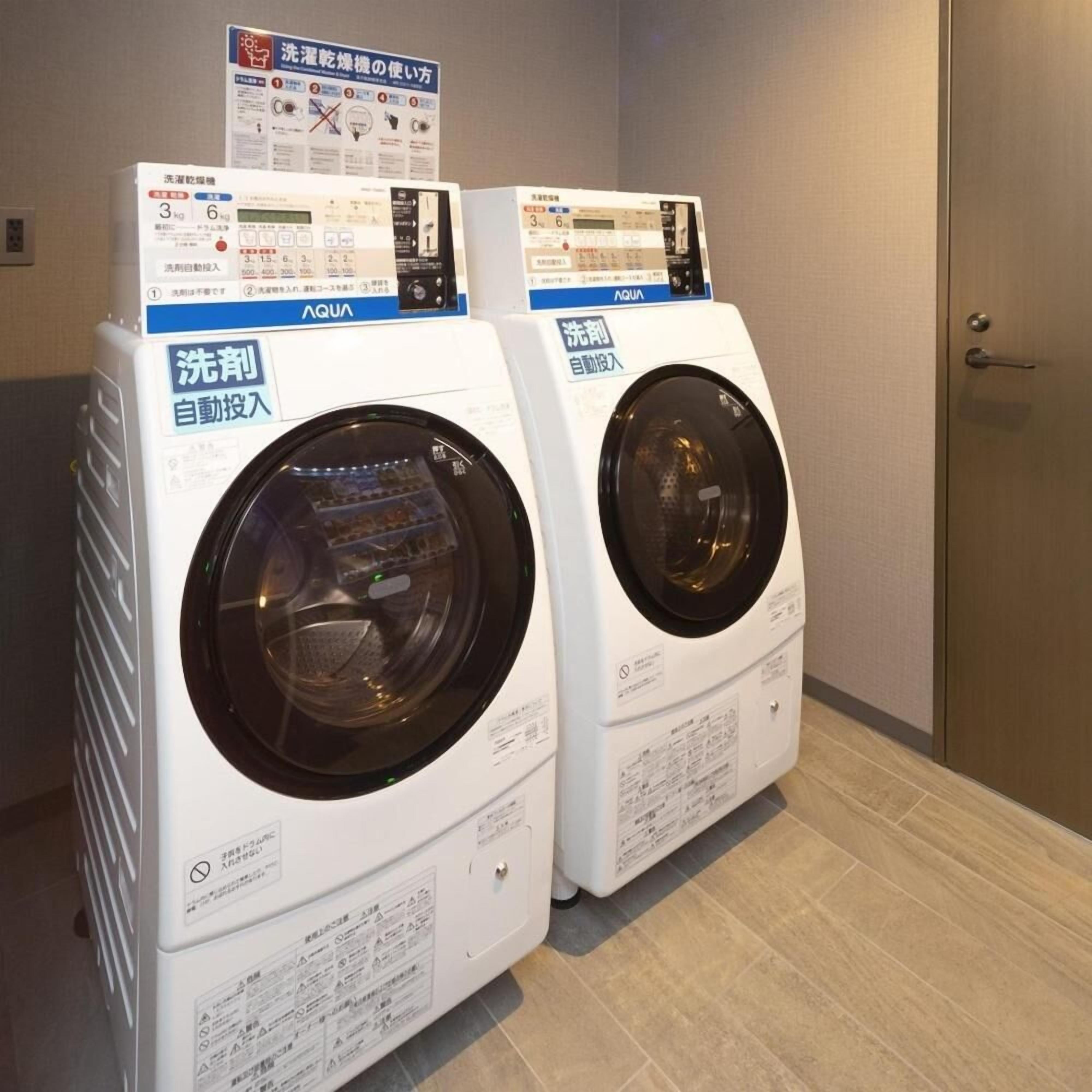 Two front-loading washing machines in a room with tiled flooring and a door on the right.