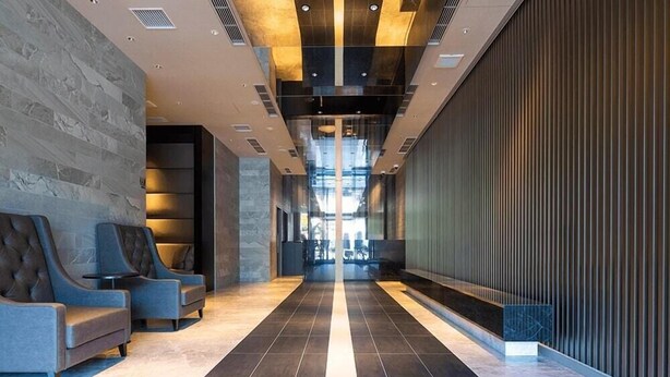 En moderne lobby med mørkt flisegulv, siddeområder med polstrede stole og en glasvæg.