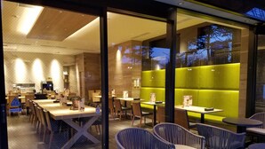 En moderne restaurant med glasafskærmning, træborde og grønne polstrede siddeområder.