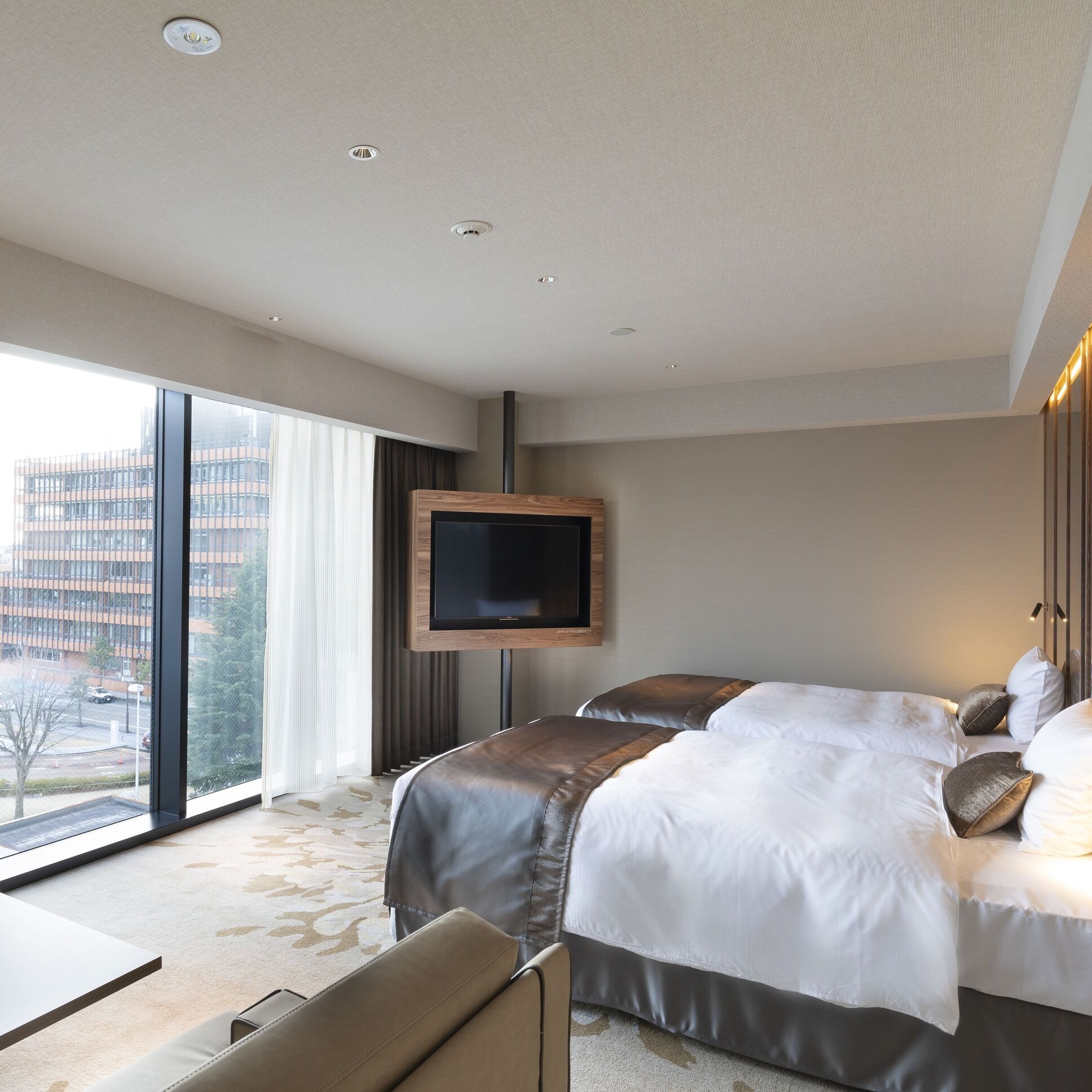 A hotel room with a large bed, a TV mounted on the wall, and a view of a cityscape through the window.