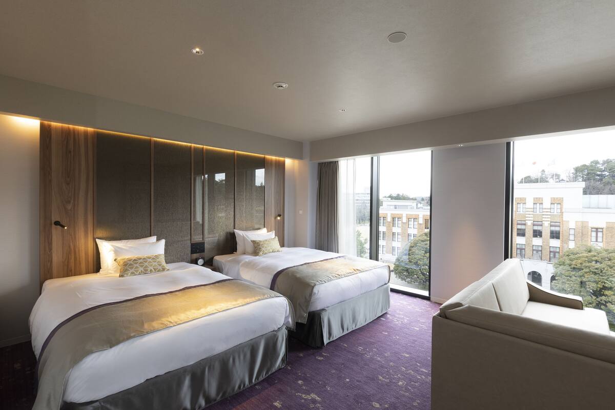 A hotel room with two beds, a large window, and a view of the city.