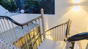 A staircase with metal railings and a handrail, leading to an outdoor area with a white wall and a window. - Floral Hotel Yi Shu Yu She Zhouzhuang (Suzhou)