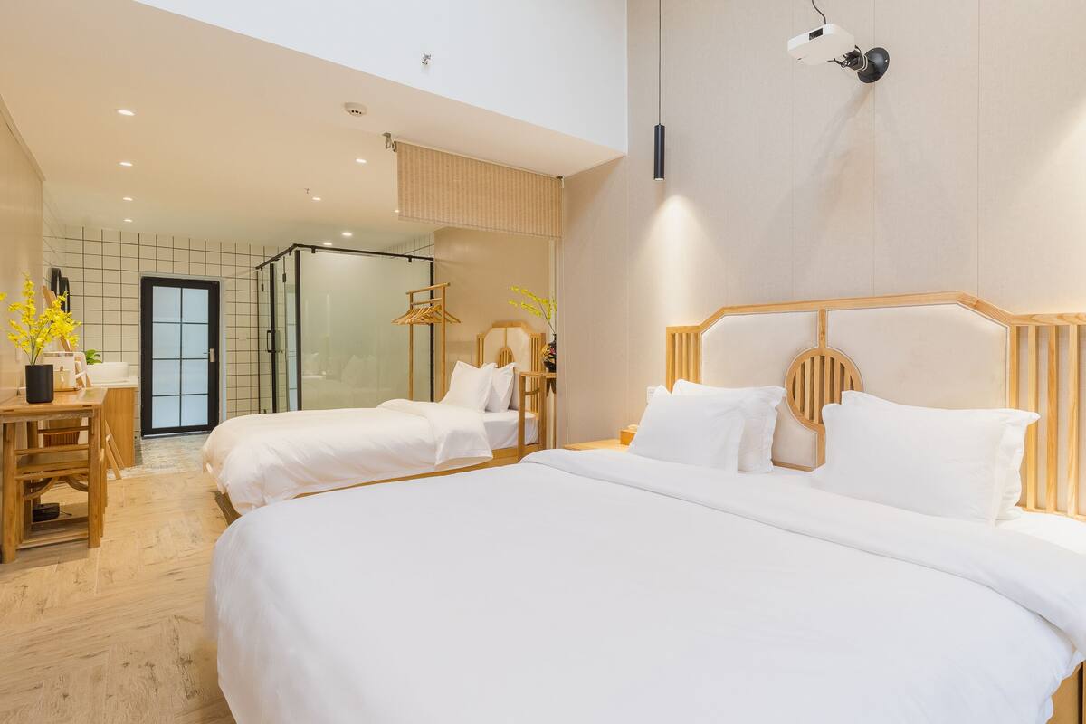Ein modernes Hotelzimmer mit zwei Betten, einem Schreibtisch und einem im Hintergrund sichtbaren Badezimmer.