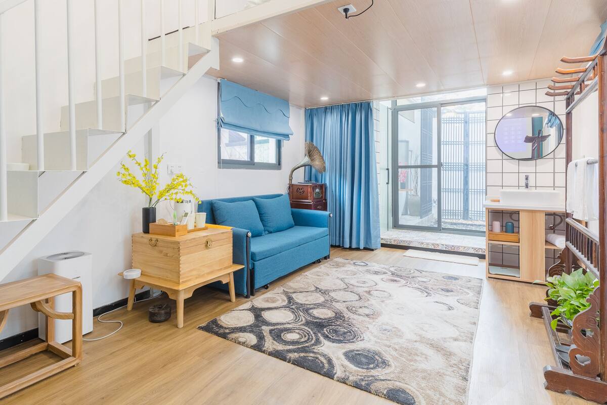 Ein modernes Wohnzimmer mit Treppe, einem blauen Sofa, einer Holzkommode und einem gemusterten Teppich.