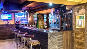 Een bar met een toonbank, krukken en een televisiescherm.