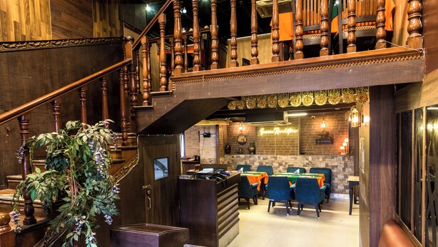 Een hotelhal met een houten trap, een receptiebalie en een eetgedeelte met blauwe stoelen.