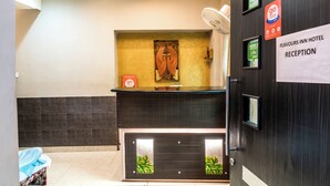 Een receptiezone met een donker houten receptiebalie, een wand met een gouden textuur, en een bordje met daarop Receptie Hotel Flavours Inn.