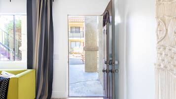 Una habitación con un sofá amarillo, una puerta que da al exterior y vistas a un edificio con balcón.