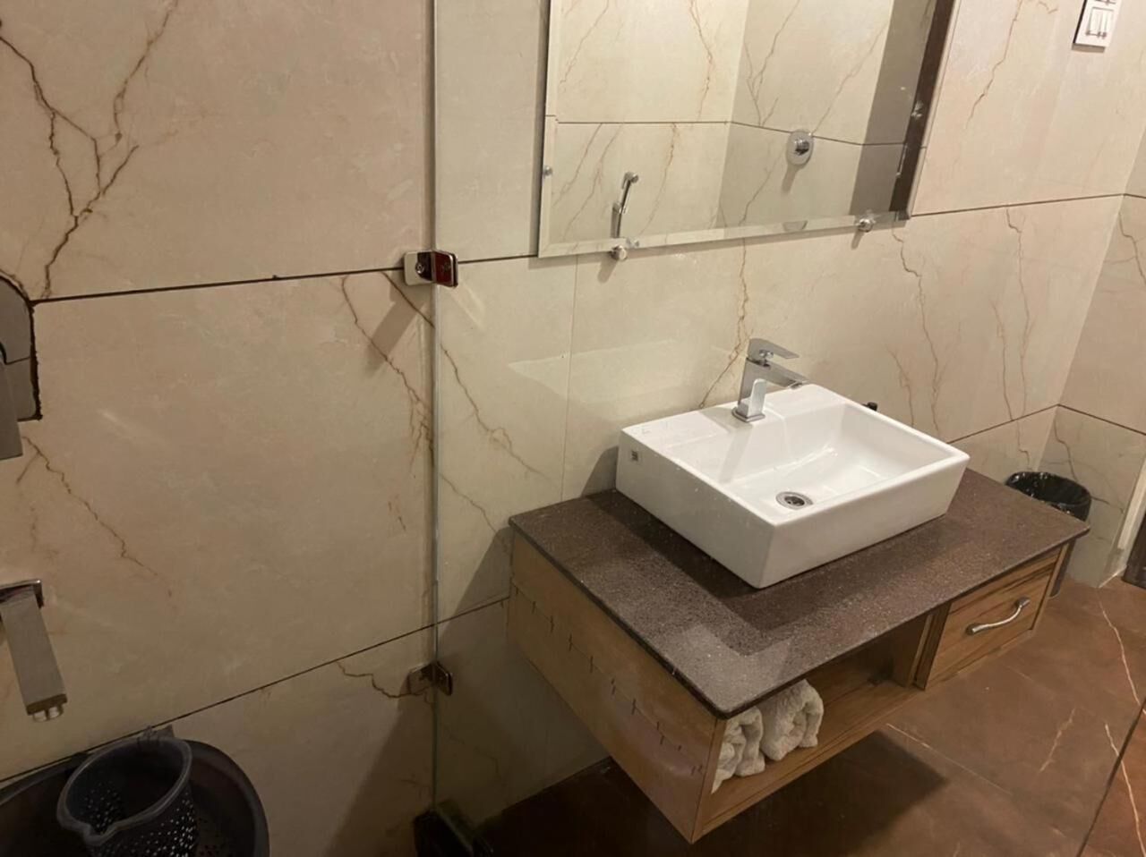A bathroom with a marble wall, a white sink, and a wooden vanity with a towel rack.