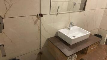 A bathroom with a marble wall, a white sink, and a wooden vanity with a towel rack.